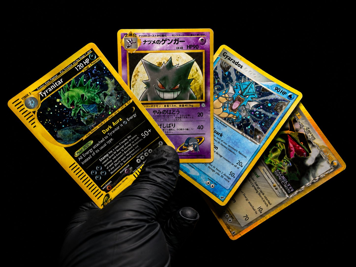 Gloved hands holding several trading cards against a black background